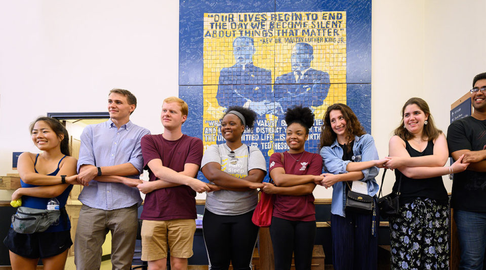 Grad students holding hands in front of mosaic of Dr. Martin Luther King, Jr. and Father Hesburgh