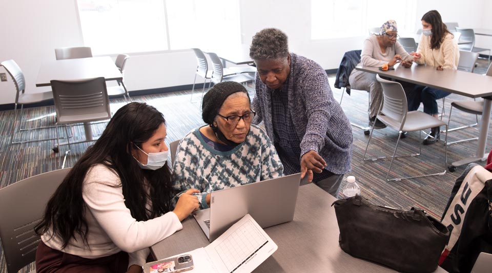 Student from Professor Kumar’s class helping an older community member with her laptop.