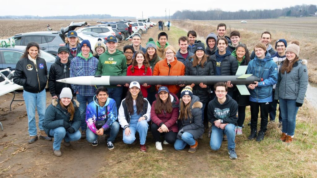 Notre Dame Rocketry group holding their rocket at the launch site